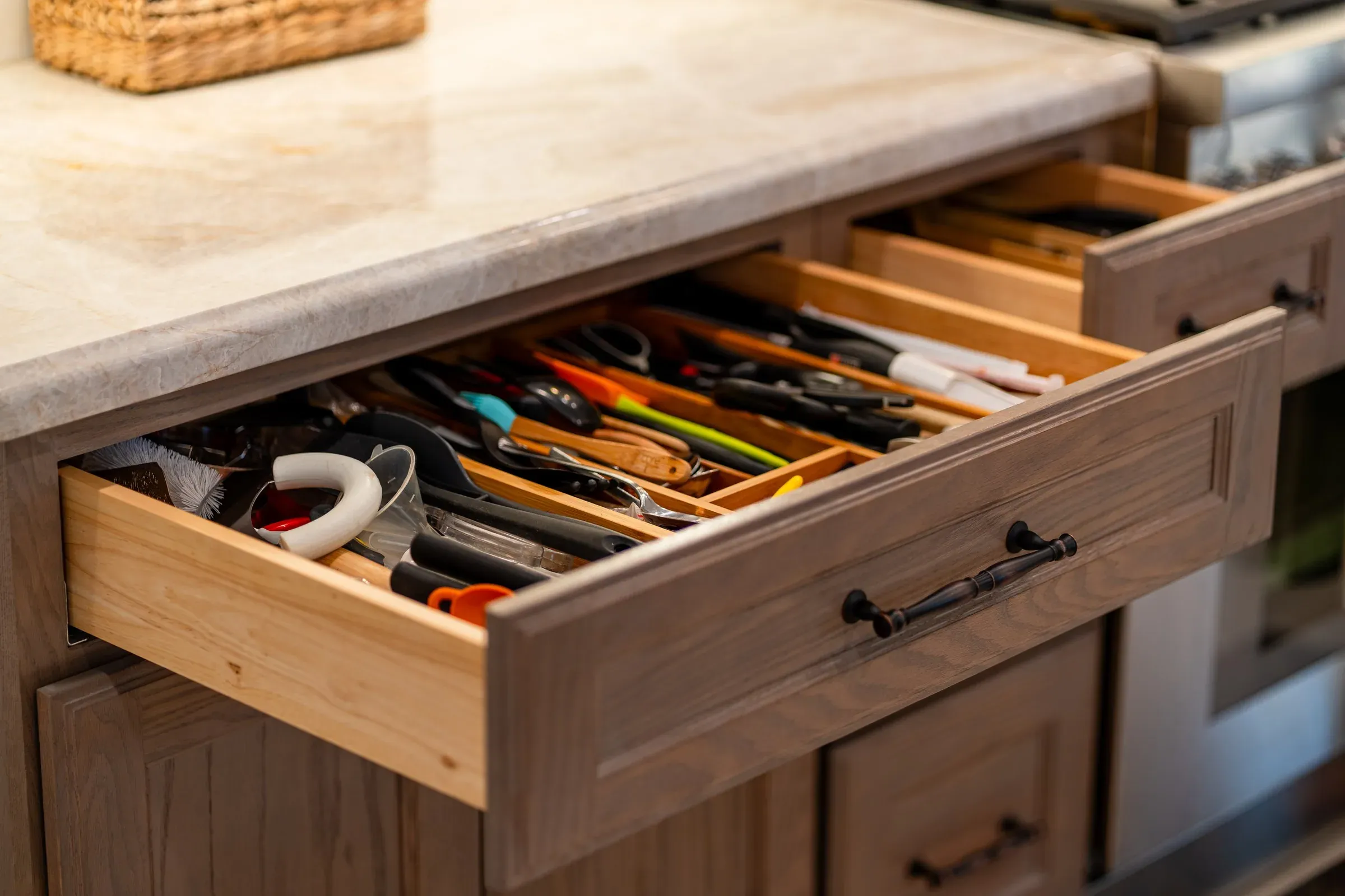 Open oak drawer with a wooden utensil divider under a stone countertop