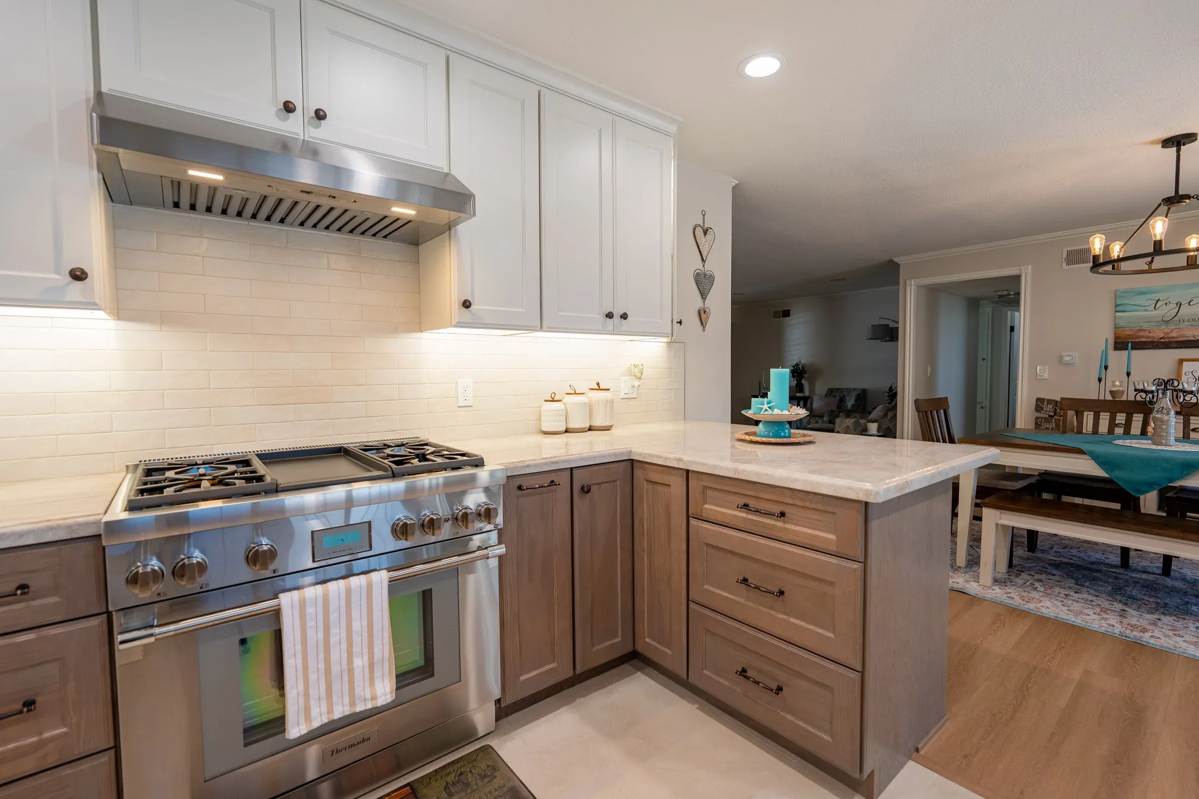 Westminster kitchen after the remodel: a stainless pro range under white wall cabinets, with stained oak base cabinets turning into a peninsula open to the dining room