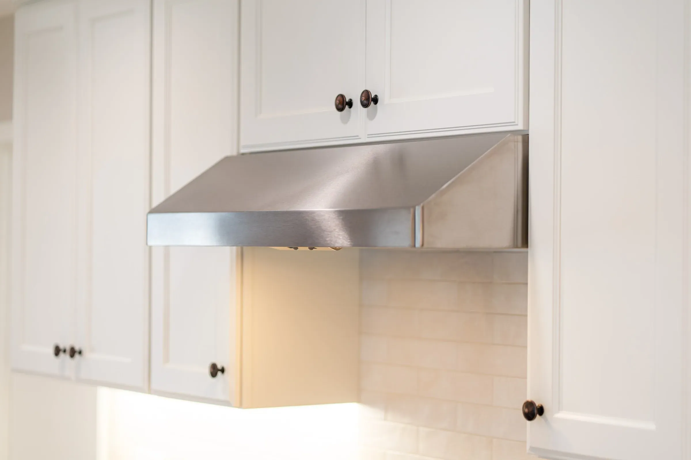 White painted upper cabinets with bronze knobs around a stainless hood and cream tile