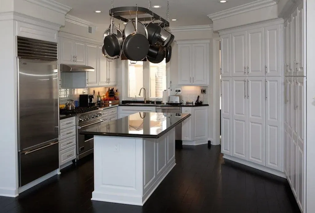 White kitchen with a pot rack above a dark-topped island and a stainless range