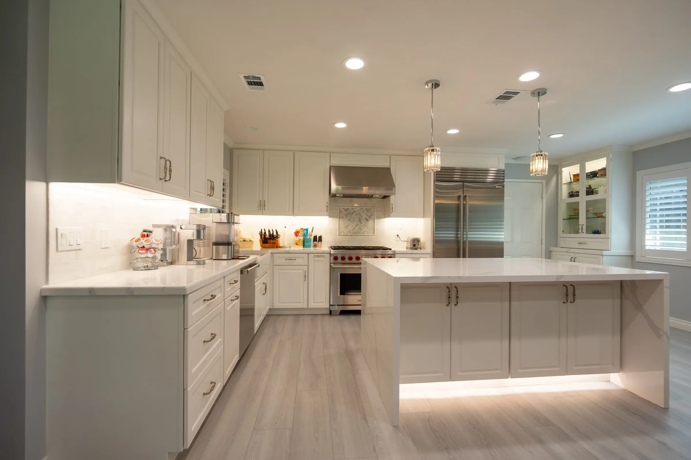 White L-shaped kitchen with a lit quartz waterfall island in the middle of the room