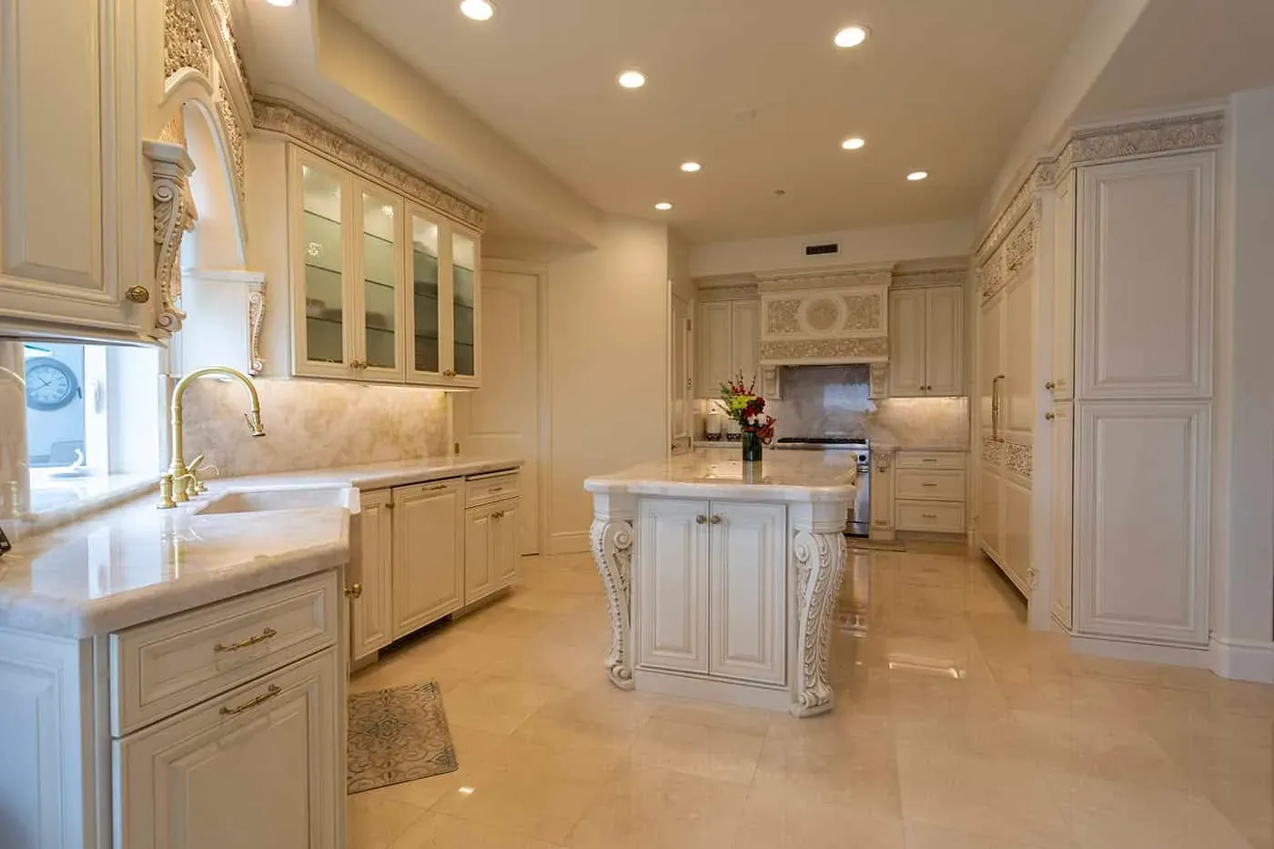 Wide view of a carved cream kitchen island and glass-front cabinets