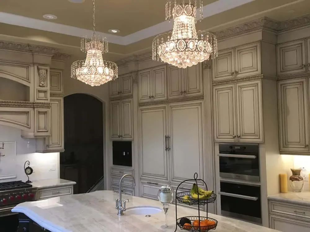 Ornate kitchen with paired chandeliers above the island and glazed cabinetry