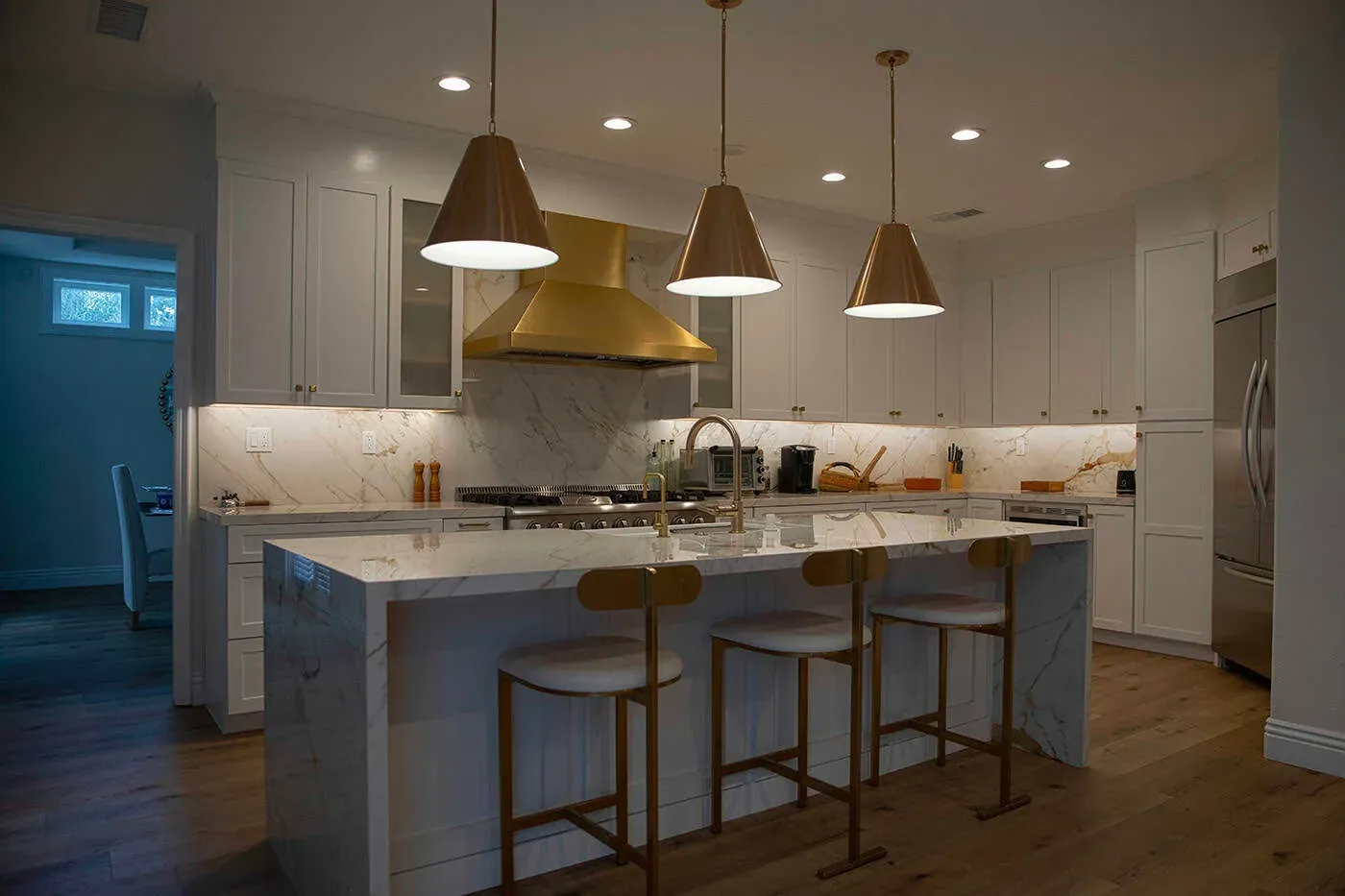 Yorba Linda kitchen with a brass hood, pendant lights and a marble waterfall island
